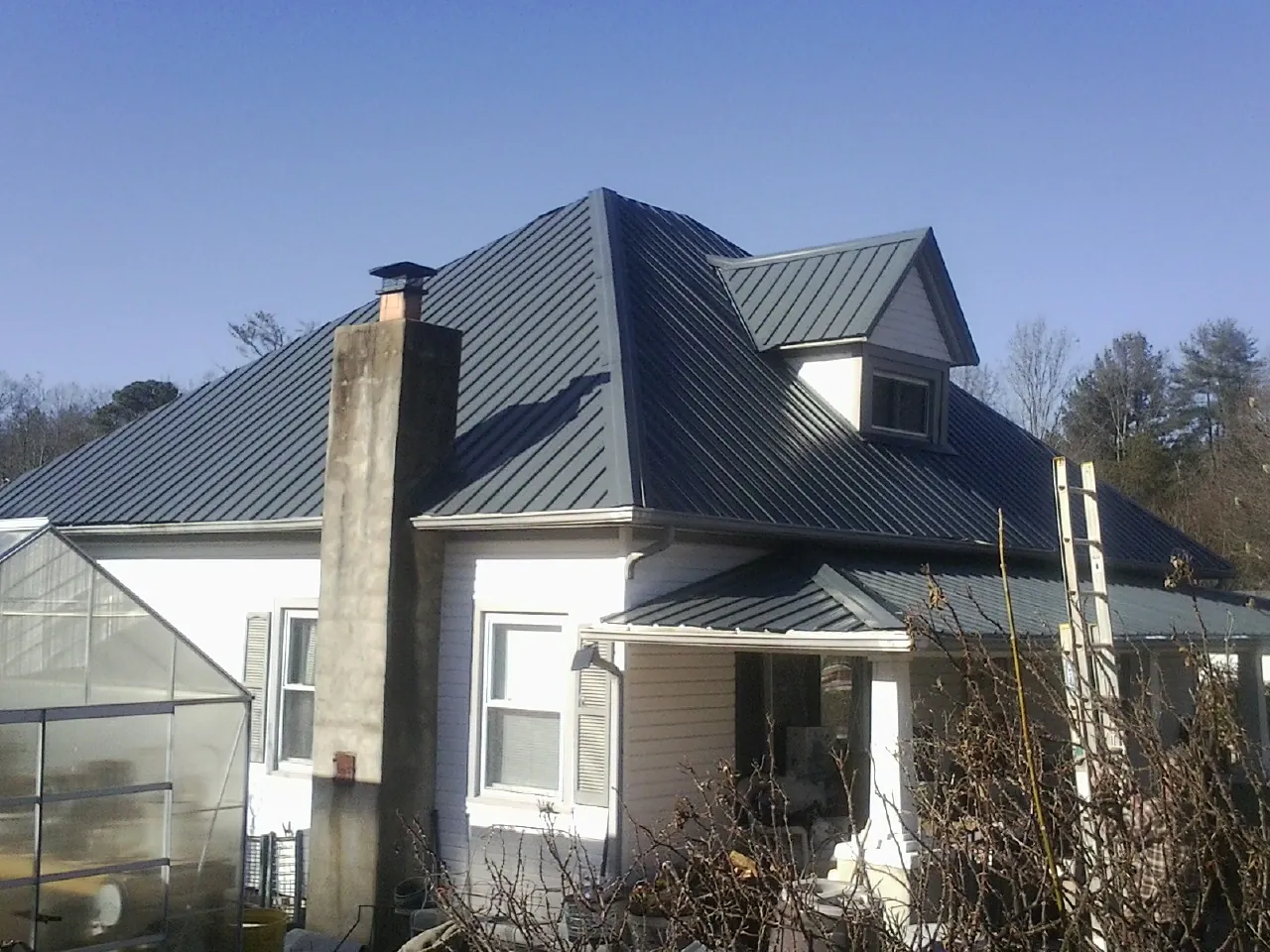 Dark blue standing seam metal roof on a white farmhouse with dormer — Slate & Tile Roof Repair by Roofing Brothers in Falkville