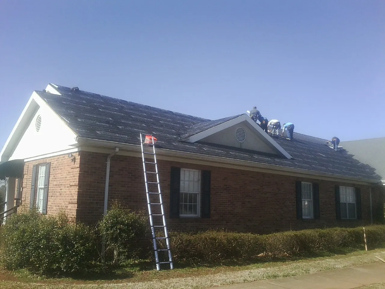 Crew tearing shingles off a brick ranch roof with a ladder set — Emergency Roof Repair work by our crew in Falkville