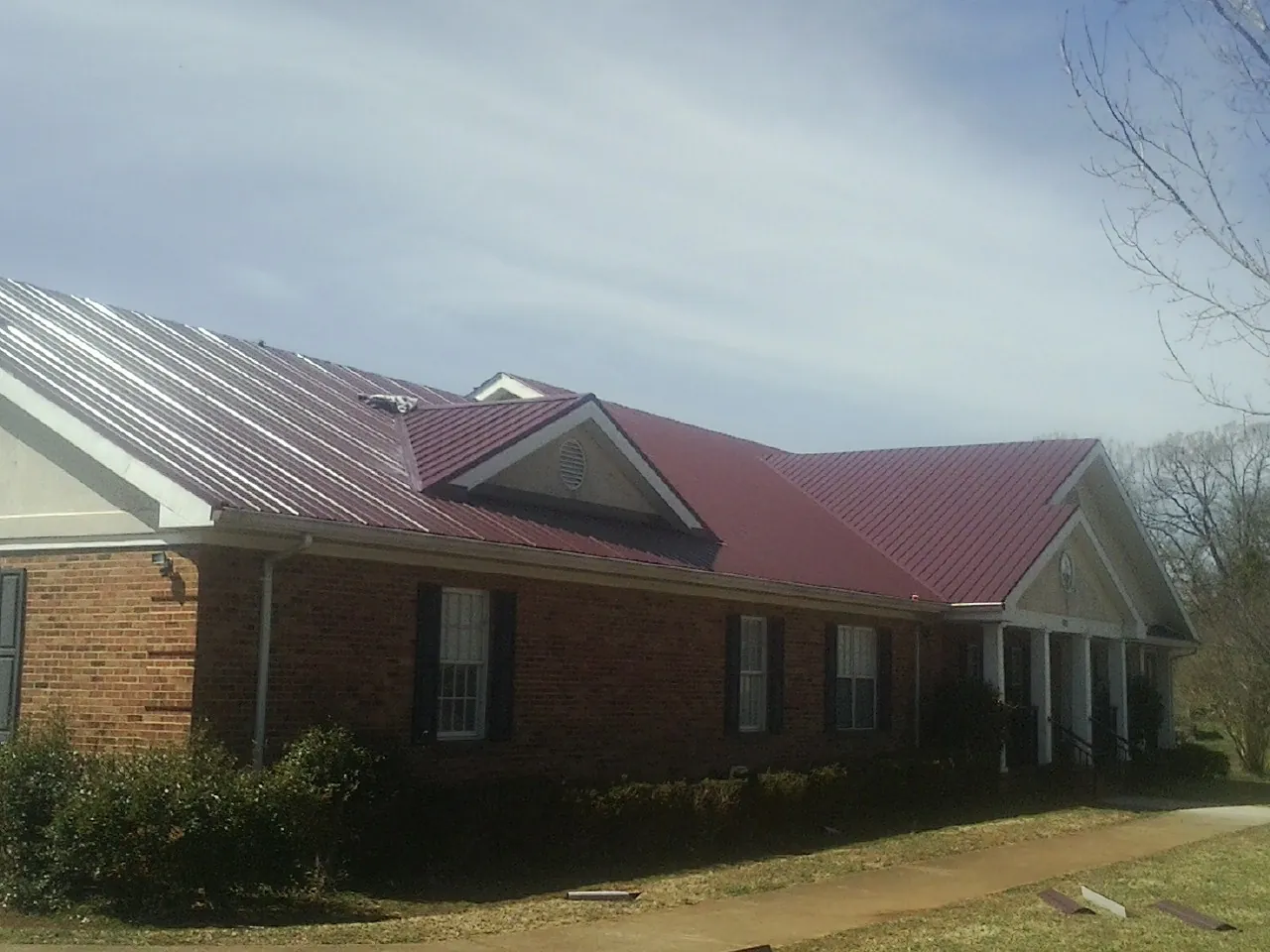 Red metal roof with gabled entries on a long brick building, from a Hail Damage Roof Repair job in Falkville