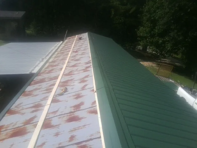 Old rusted panels beside newly installed green metal roofing — Wind Damage Roof Repair by Roofing Brothers in Falkville