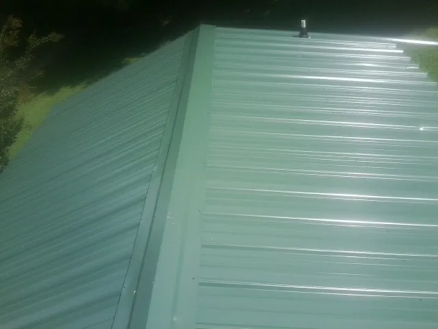 New green metal panels meeting at the ridge of a roof — Flat Roof Repair work by our crew in Falkville