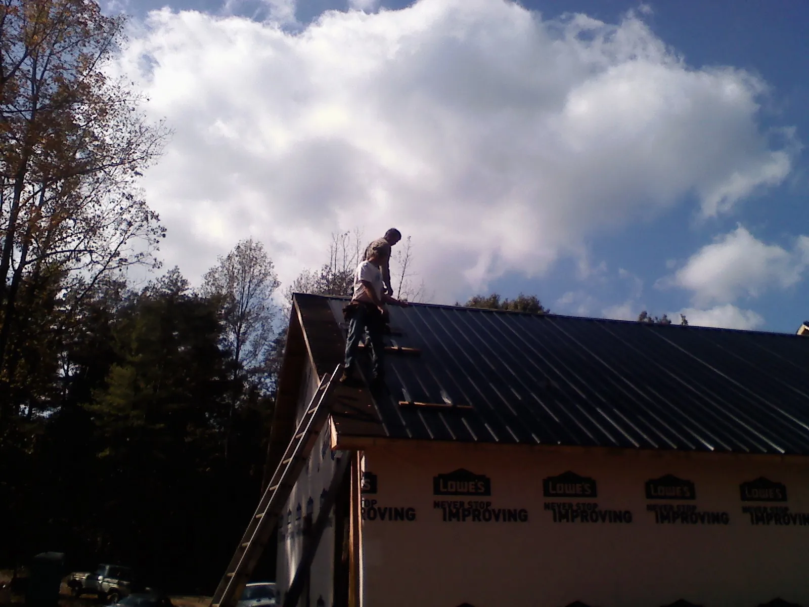 Roofer fastening dark metal panels high against a cloudy sky, from a Roof Inspection job in Falkville