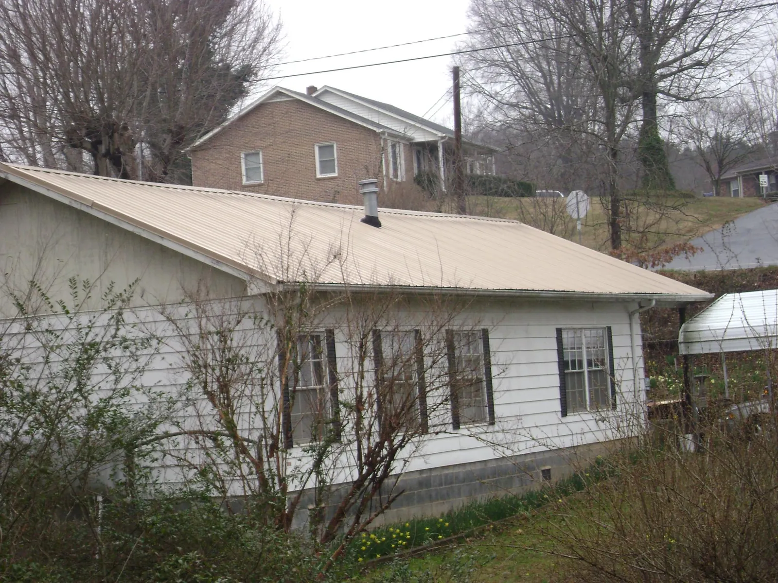 Tan metal roof on a white sided house set into a hillside — Commercial Roofing by Roofing Brothers in Falkville