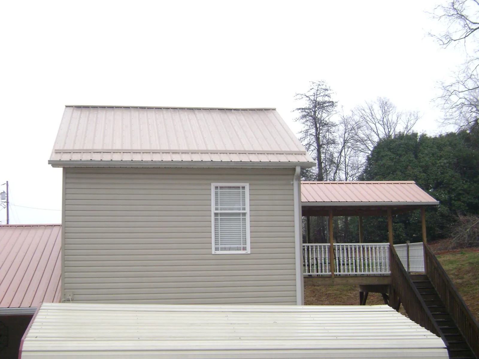 Tan metal roofs on a two story addition and attached porch, from a Roof Replacement job in Falkville